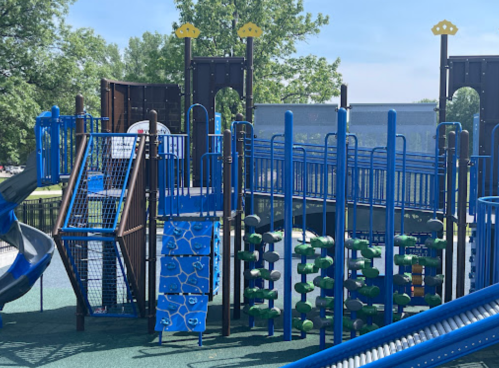 Colorful playground equipment with slides, climbing structures, and interactive panels in a sunny park setting.
