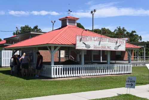 A red-roofed pavilion with a sign reading "World's Largest Frying Pan" in Rose Hill, NC, with people gathered outside.