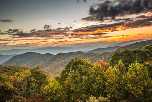 A scenic view of mountains at sunset, with vibrant colors and lush trees in the foreground.