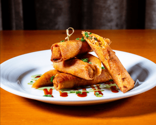 A plate of crispy spring rolls garnished with green onions and drizzled with sauce, stacked artfully.