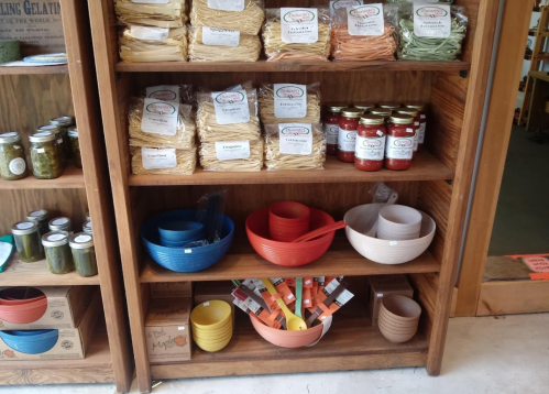 A wooden shelf displaying various pasta packages, jars of sauce, and colorful bowls in different sizes.