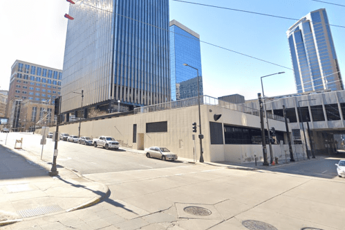 City street view featuring modern buildings, parked cars, and clear blue skies.
