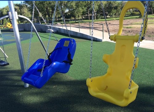 Two swings in a playground: one blue and one yellow, hanging from chains on a green rubber surface.