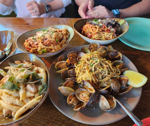 A table with four dishes: pasta with clams, spaghetti, and two other pasta dishes, garnished and ready to eat.