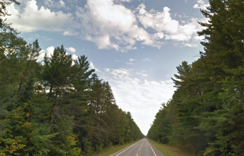 A straight road lined with tall trees under a partly cloudy sky.
