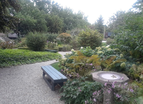 A serene garden path winding through lush greenery and blooming flowers, with a bench and a birdbath nearby.