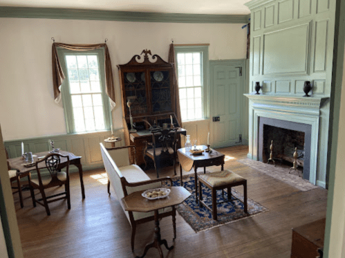 A cozy, vintage room with a fireplace, wooden furniture, and large windows letting in natural light.