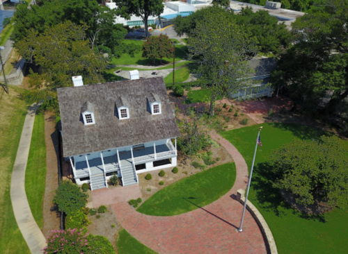 Aerial view of a historic house surrounded by greenery and pathways, with a flagpole in the foreground.