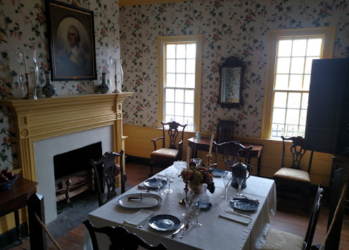 A vintage dining room with floral wallpaper, a fireplace, and a table set for a meal.