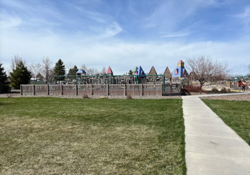 A playground with colorful structures surrounded by grass and trees, with a pathway leading towards it.