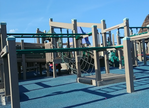 A playground structure with climbing features and slides, set against a clear blue sky.
