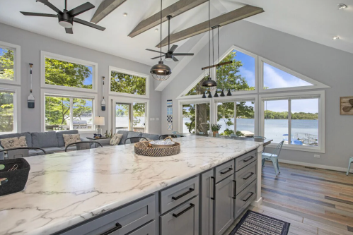 Bright kitchen with a marble island, large windows, and a view of the lake, featuring modern decor and natural light.