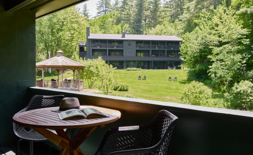 A balcony view of a green landscape with a gazebo, chairs, and a hotel in the background surrounded by trees.