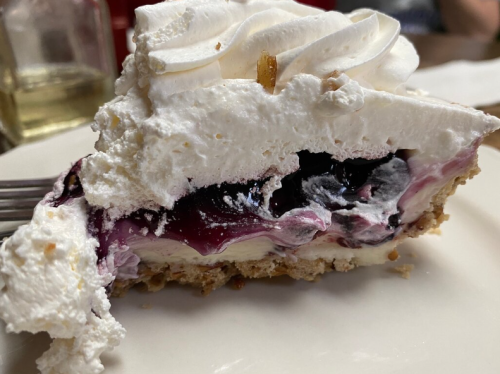 A slice of pie with a creamy filling, topped with whipped cream and a layer of berry sauce, on a white plate.