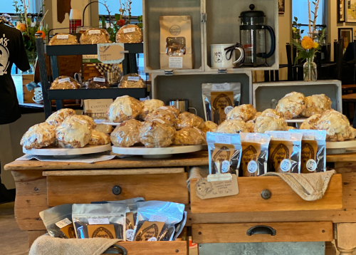 A display of freshly baked pastries and packaged goods on a wooden table in a cozy café setting.
