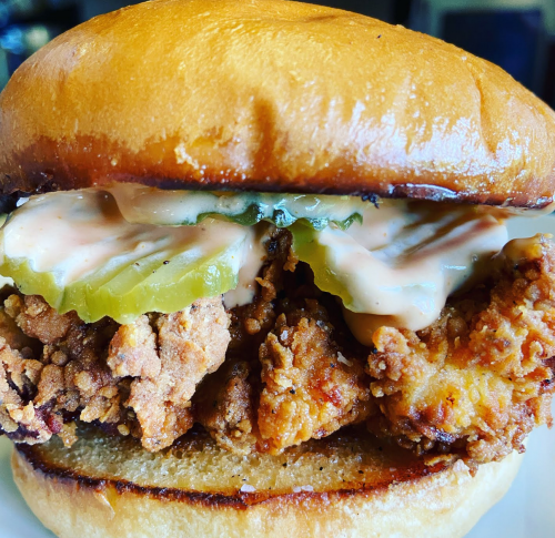 A close-up of a crispy fried chicken sandwich with pickles and sauce on a toasted bun.