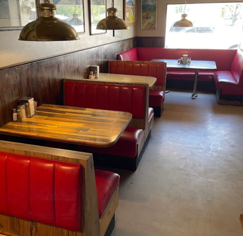 Cozy diner interior with red booths, wooden tables, and large windows letting in natural light.