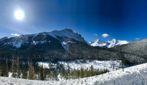 A panoramic view of snow-covered mountains under a clear blue sky, with the sun shining brightly.