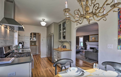 A modern kitchen with a chandelier, stainless steel appliances, and a dining area leading to a cozy living room.
