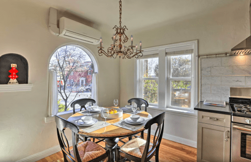 Cozy dining area with a round table set for four, a chandelier, and large windows letting in natural light.