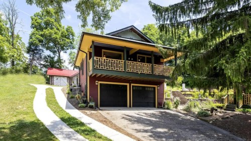 A modern two-story house with a yellow and black exterior, featuring a driveway and surrounded by greenery.