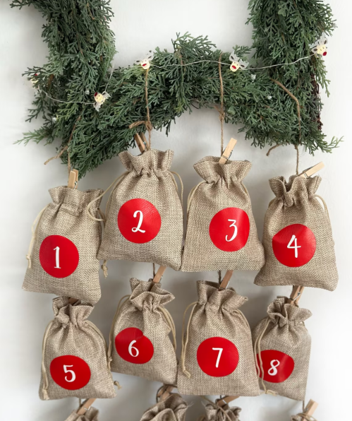 A festive display of burlap bags numbered 1 to 8, hanging on a green garland.