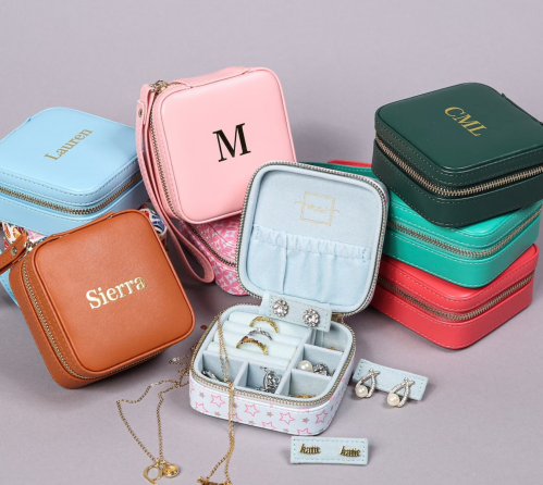 Colorful personalized jewelry cases in various sizes, featuring names and initials, arranged on a gray background.