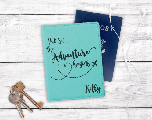 A teal passport holder with "And so... the Adventure begins" and "Kelly" next to a blue passport and keys.