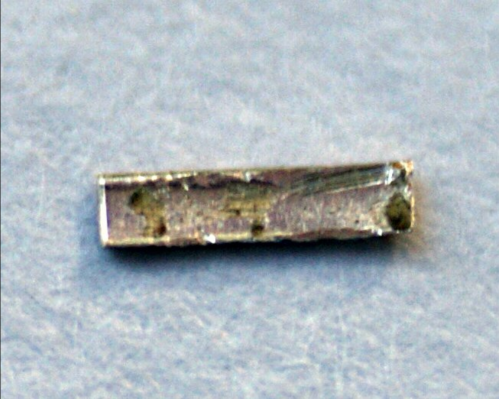 A small, rectangular metallic object with a shiny surface, resting on a light blue background.