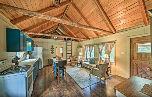 Cozy cabin interior with wooden beams, a kitchen, living area, and spiral staircase, featuring warm lighting and rustic decor.