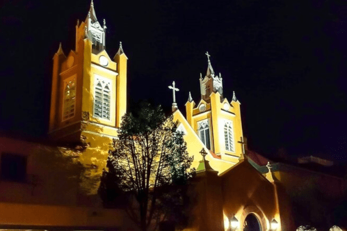 A brightly lit church at night, featuring two tall towers and illuminated crosses against a dark sky.