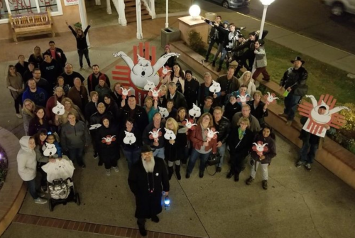 A large group of people poses together outdoors, holding up playful signs with cartoon characters.