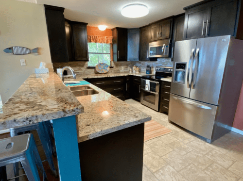 Modern kitchen with dark cabinets, stainless steel appliances, and a granite countertop, featuring a blue island and tile flooring.