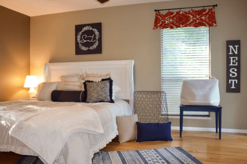 Cozy bedroom with a white bed, decorative pillows, a nightstand, and a window with natural light.