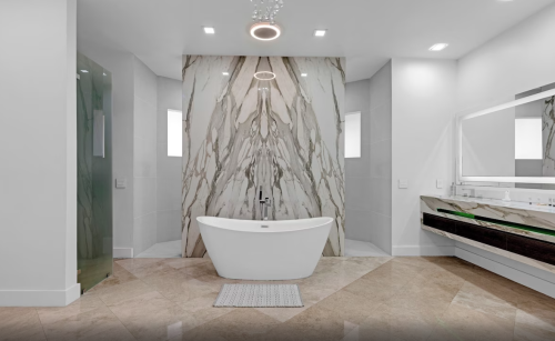 Modern bathroom featuring a freestanding tub, marble accent wall, and sleek vanity with a large mirror.