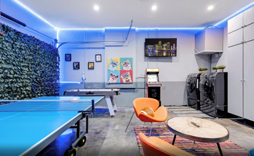 A modern game room featuring a ping pong table, arcade machine, laundry area, and vibrant decor with LED lighting.