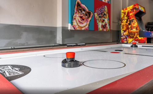 A close-up of an air hockey table with a red puck and colorful arcade game posters in the background.