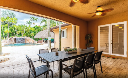 A patio with a dining table and chairs, overlooking a pool and tropical landscaping.