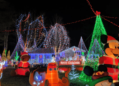 Colorful Christmas lights illuminate a yard with inflatable decorations, including a bear, cat, and Mickey Mouse, with a "Merry Christmas" sign.