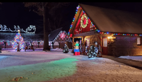 A festive scene featuring a decorated cabin, colorful lights, a Christmas tree, and snow-covered ground at night.