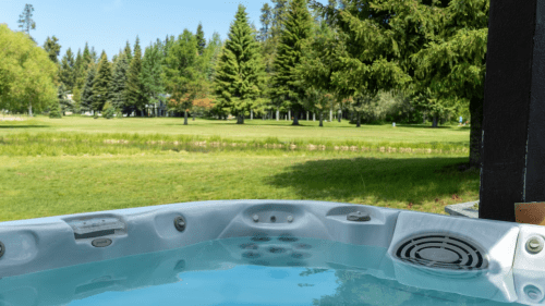 A hot tub with clear water, surrounded by lush green trees and a grassy field in the background.