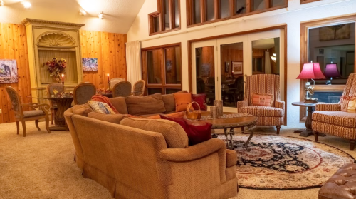 Cozy living room with a large sofa, armchairs, a coffee table, and warm lighting, featuring wooden accents and a rug.