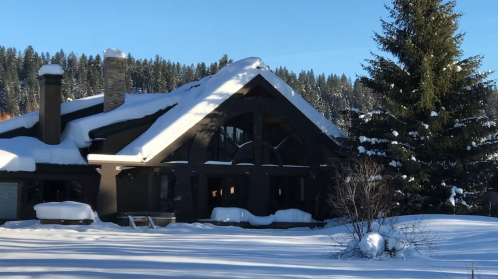 A snow-covered house surrounded by trees, with a clear blue sky in the background.