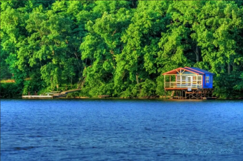 A colorful house on stilts by a serene lake, surrounded by lush green trees.