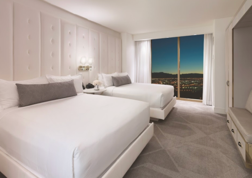 A modern hotel room with two beds, a large window showcasing a city view, and stylish decor.