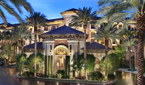 Luxurious hotel entrance surrounded by palm trees and lush greenery, illuminated at dusk.