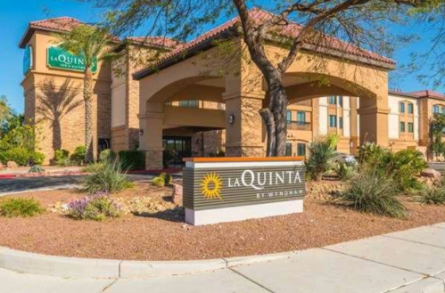 Exterior view of a La Quinta hotel with a sign, featuring desert landscaping and a sunny sky.
