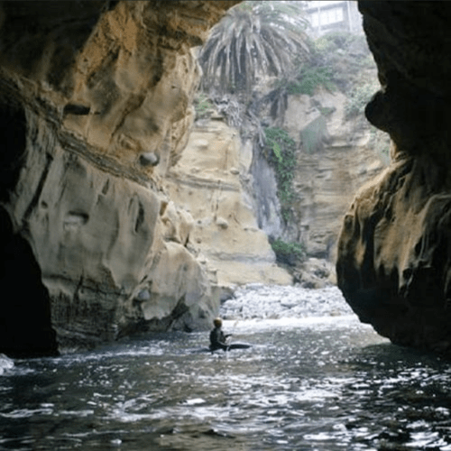 A person kayaking through a narrow canyon with steep, rocky walls and lush vegetation above.