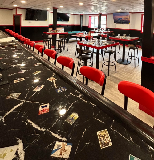 Interior of a restaurant featuring a black marble bar, red stools, and tables with a modern design.