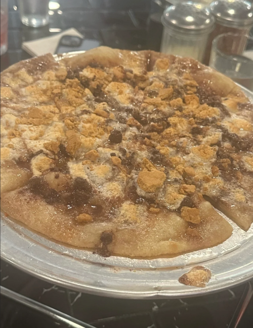 A close-up of a dessert pizza topped with crumbled cookies and a sweet glaze on a silver platter.